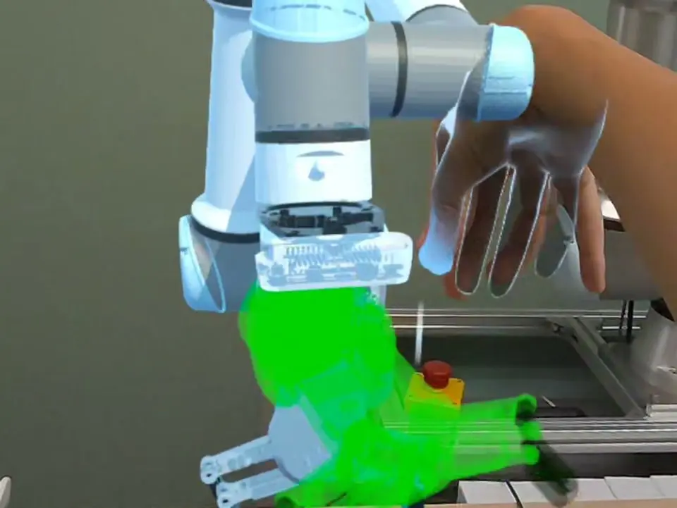 An operator's hand reaching for the green target pose of the gripper hologram
